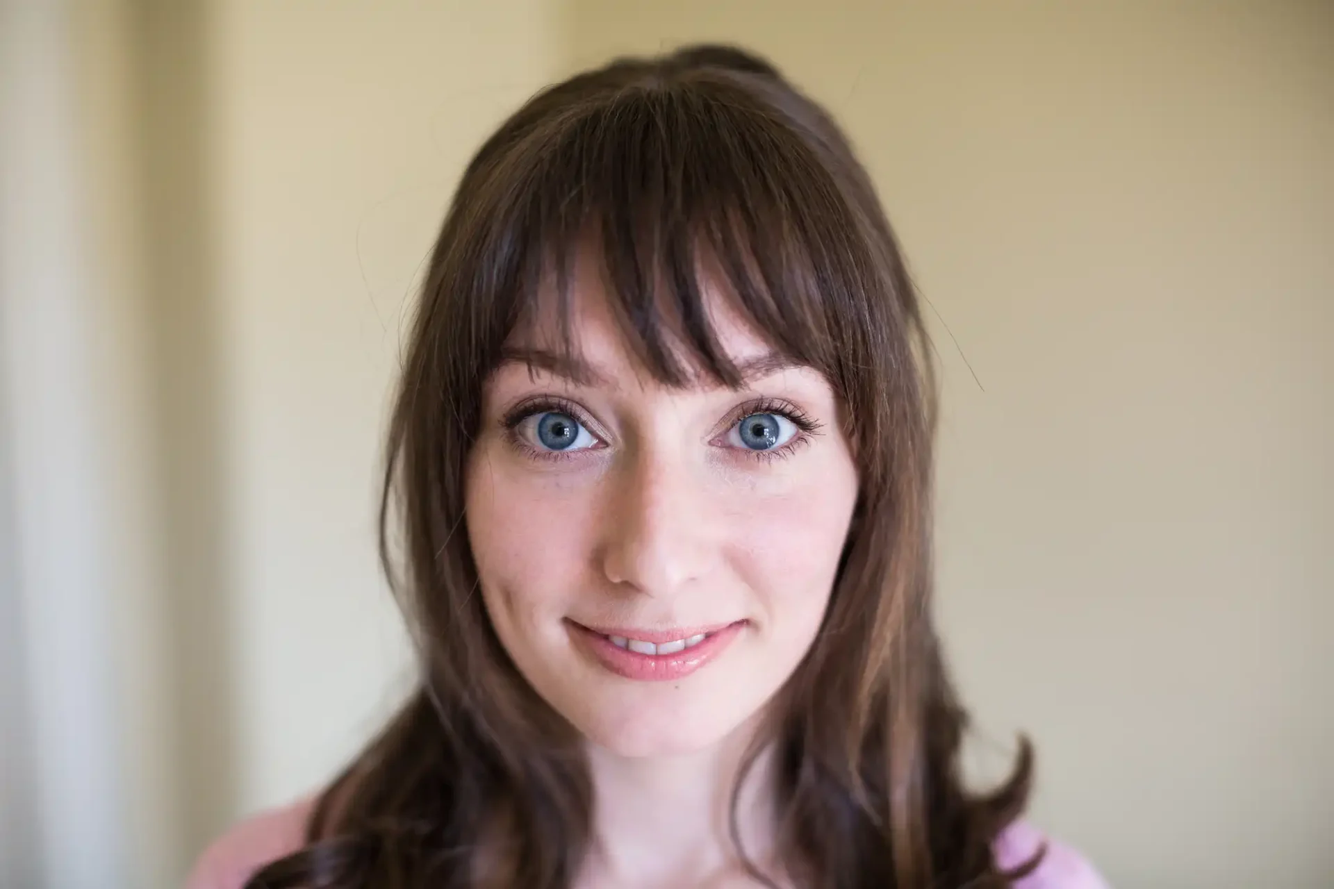 Portrait of a woman with shoulder-length brown hair and blue eyes, smiling subtly in a softly lit room.