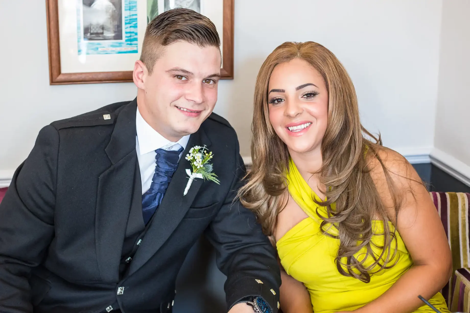 A man in a suit and a woman in a yellow dress smiling and sitting together at a formal event.