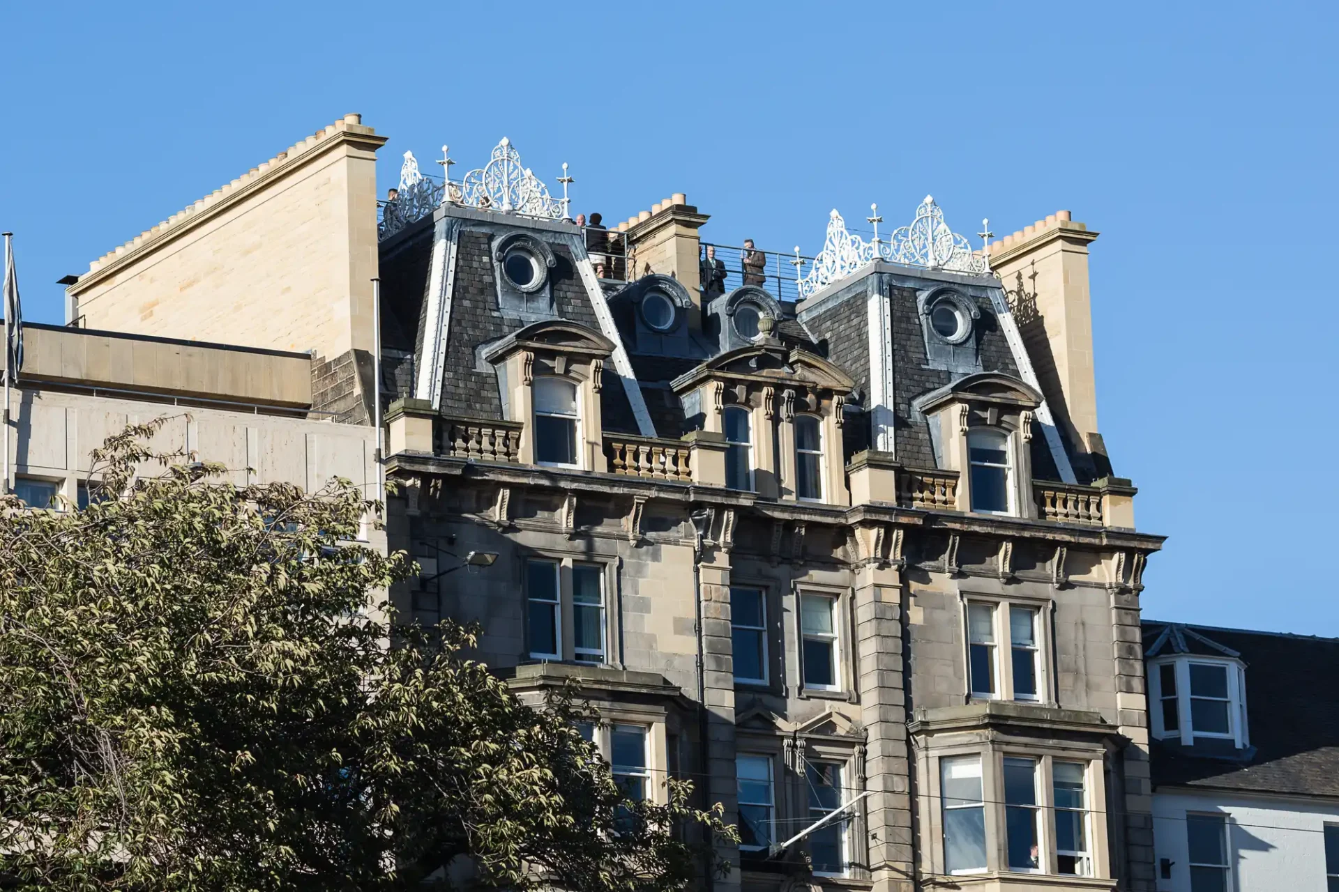Victorian building with ornate metal cresting on the roof and four dormer windows against a clear blue sky.