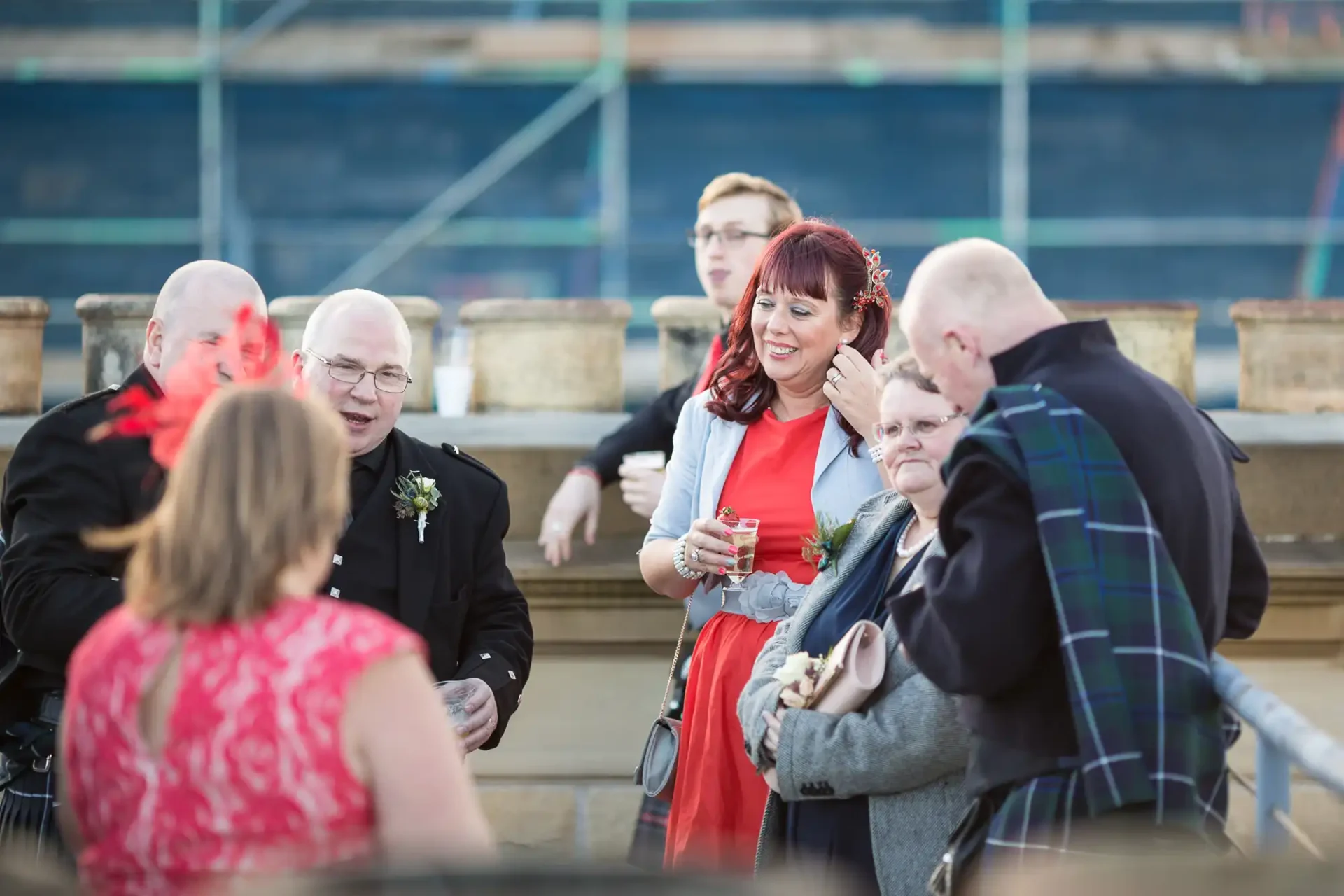 Group of adults in formal attire conversing and smiling at an outdoor event, with ambient focus and natural lighting.