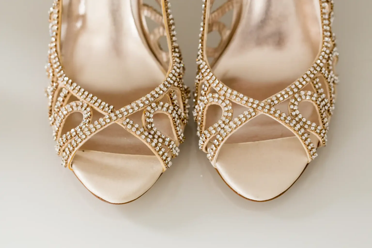A close-up of elegant gold high-heeled shoes adorned with many small crystals on a light neutral background.