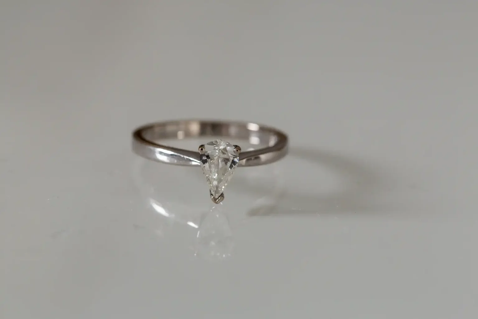 A single diamond ring with a marquise cut on a reflective white surface.
