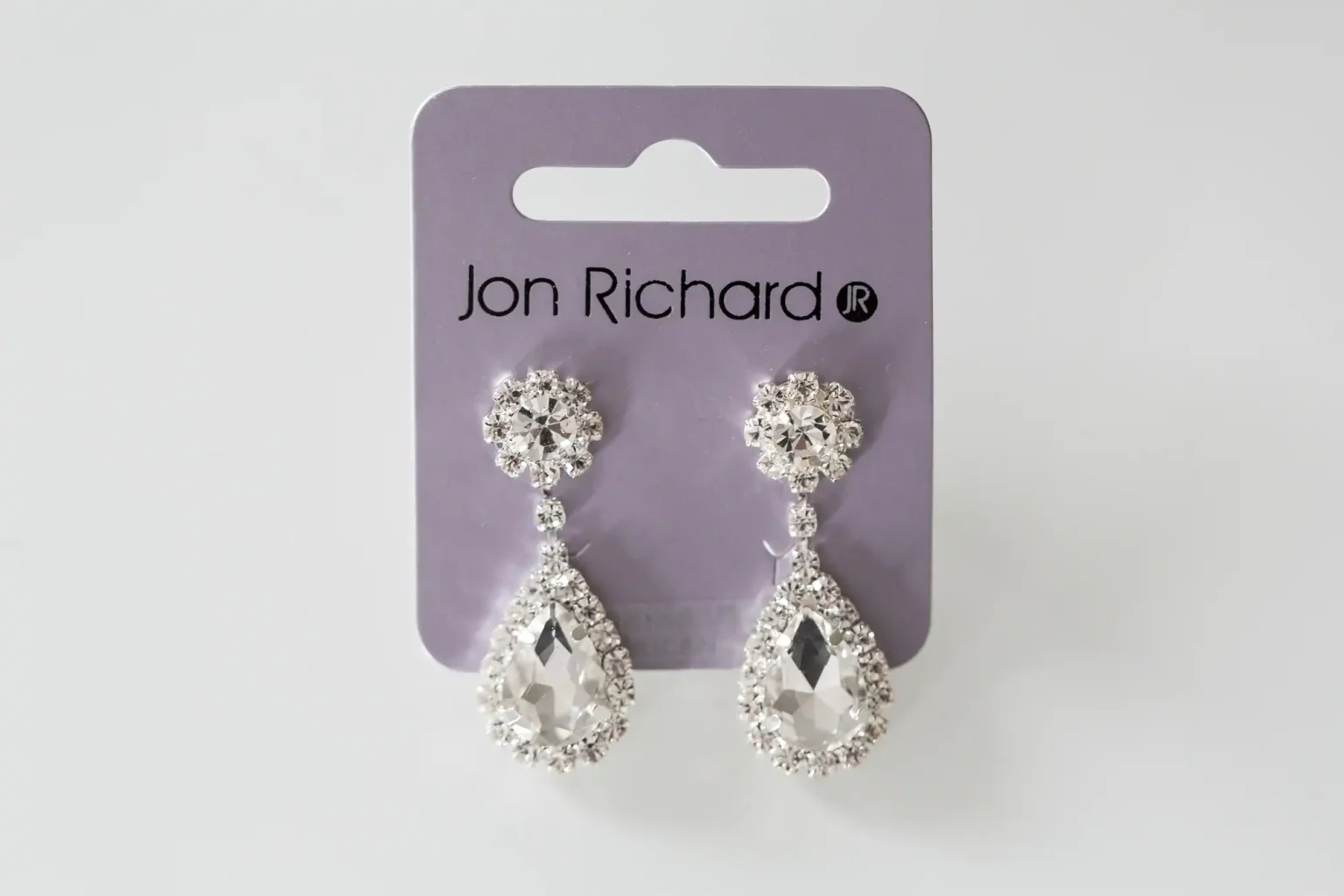 Pair of jon richard teardrop crystal earrings displayed on a branded card against a white background.