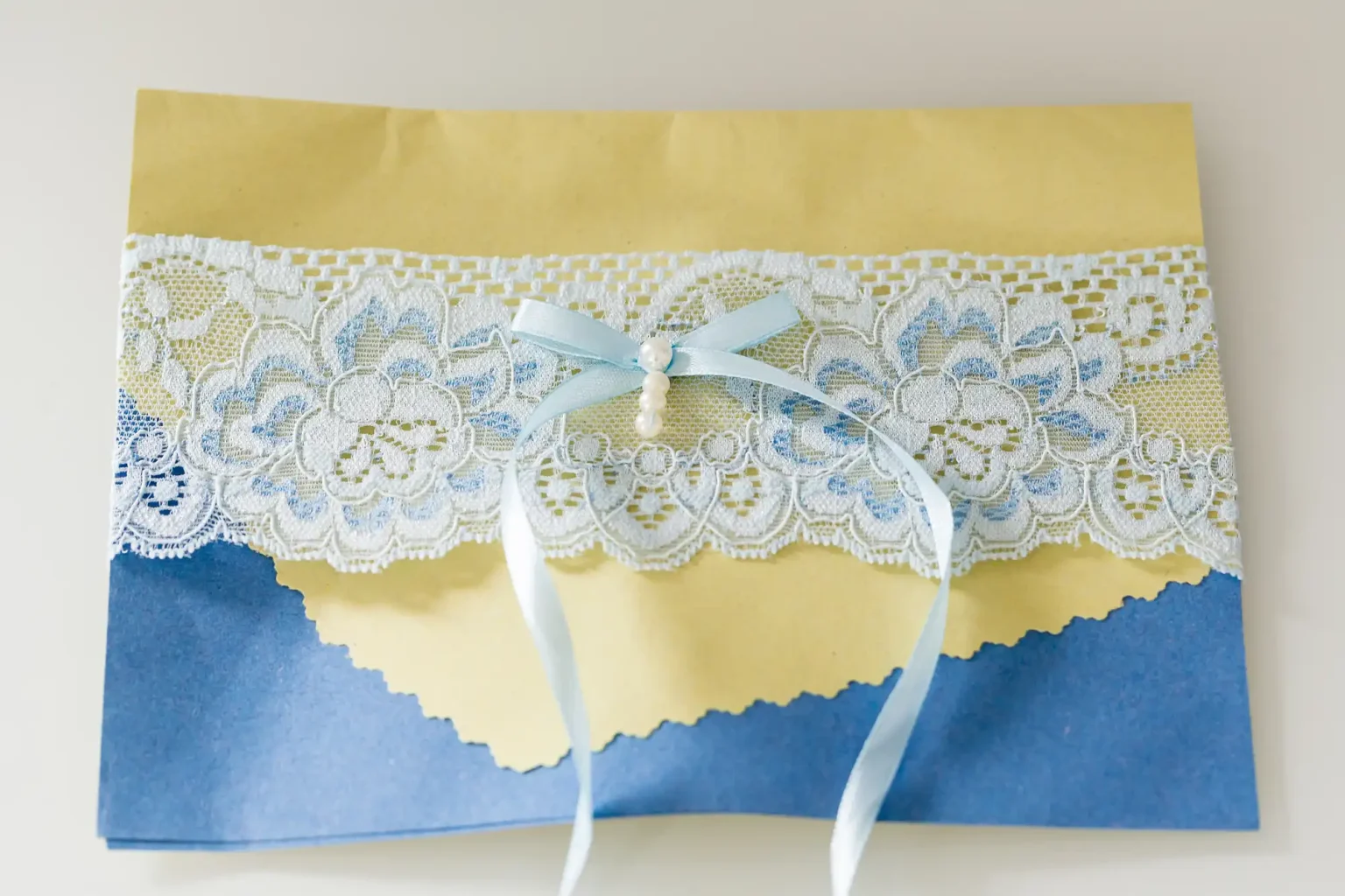 Handmade greeting card with blue and yellow torn paper layers, adorned with white lace and a blue ribbon bow.