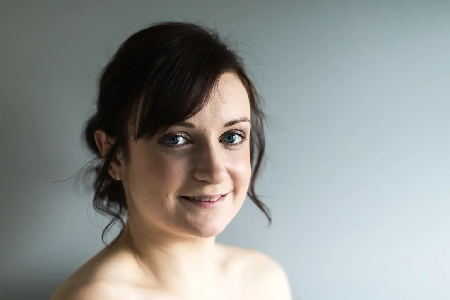 A portrait of a smiling woman with dark hair and blue eyes, posing against a plain, light gray background.