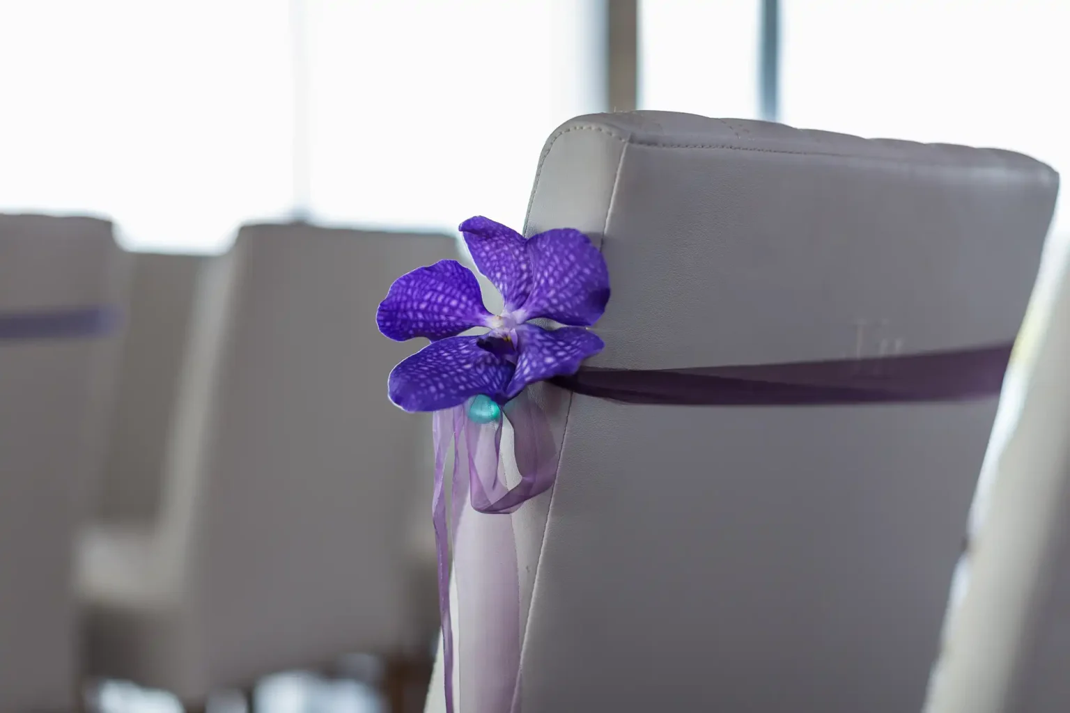 A purple flower and ribbon adorn a gray chair in a room with soft lighting, indicating a decorative or celebratory setting.