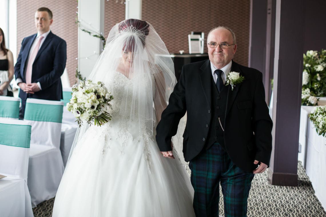 bride holding hands with her father as they walk up the aisle