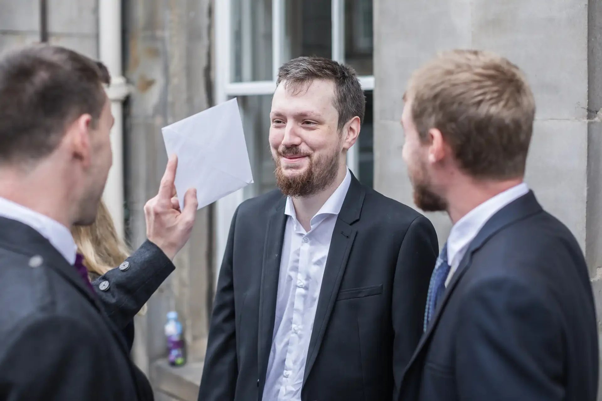Three business professionals in suits having a conversation outdoors, one man smiling and holding a document.