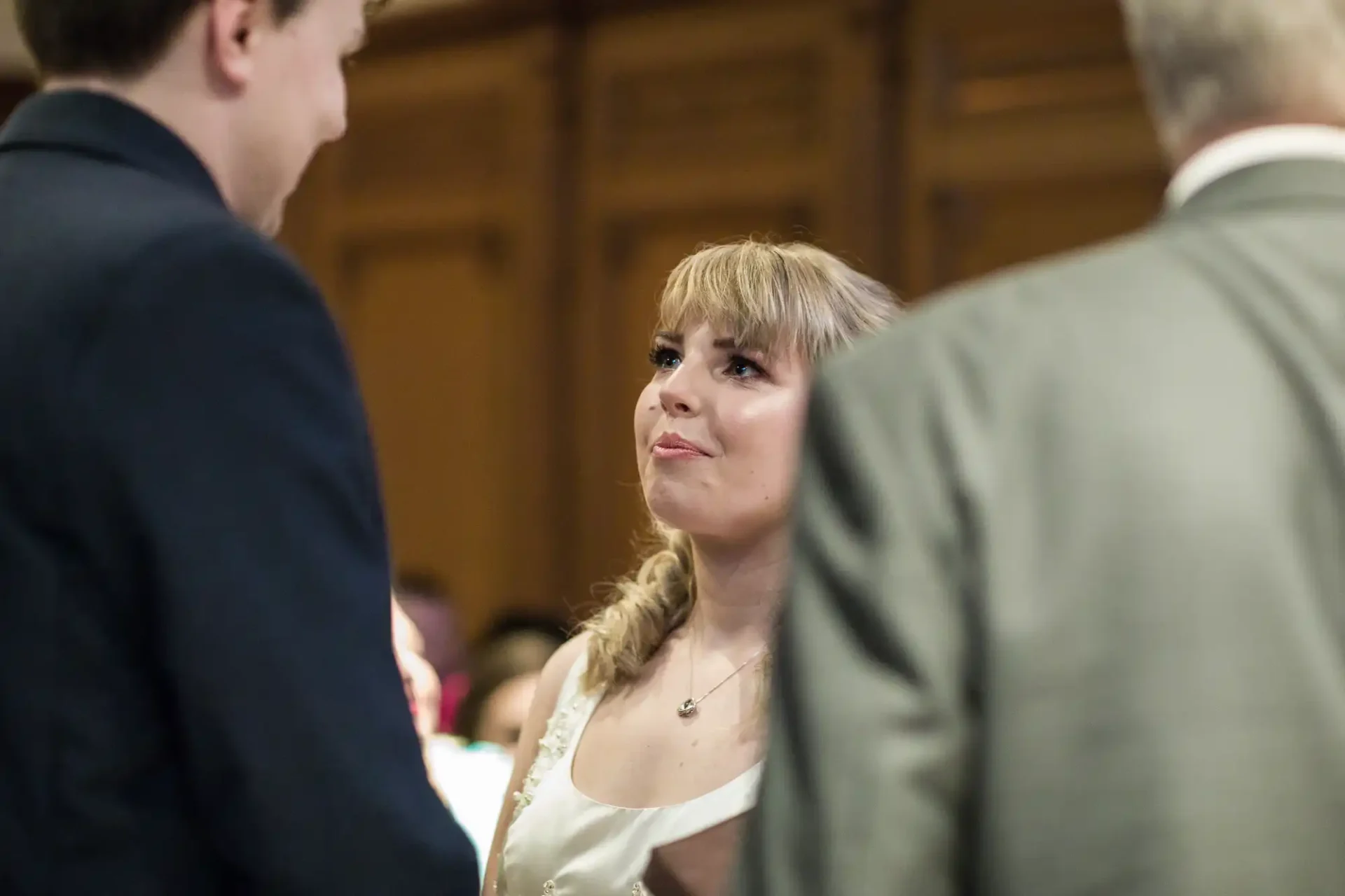 A woman with a braid listening intently to a man in a suit at a formal gathering, with another man’s back visible in the foreground.