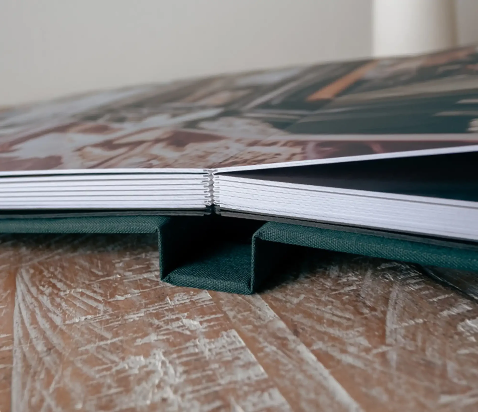 Luxury wedding photo albums Scotland: Close-up of an open photo book placed on a wooden surface, showing the binding and edges of the pages.