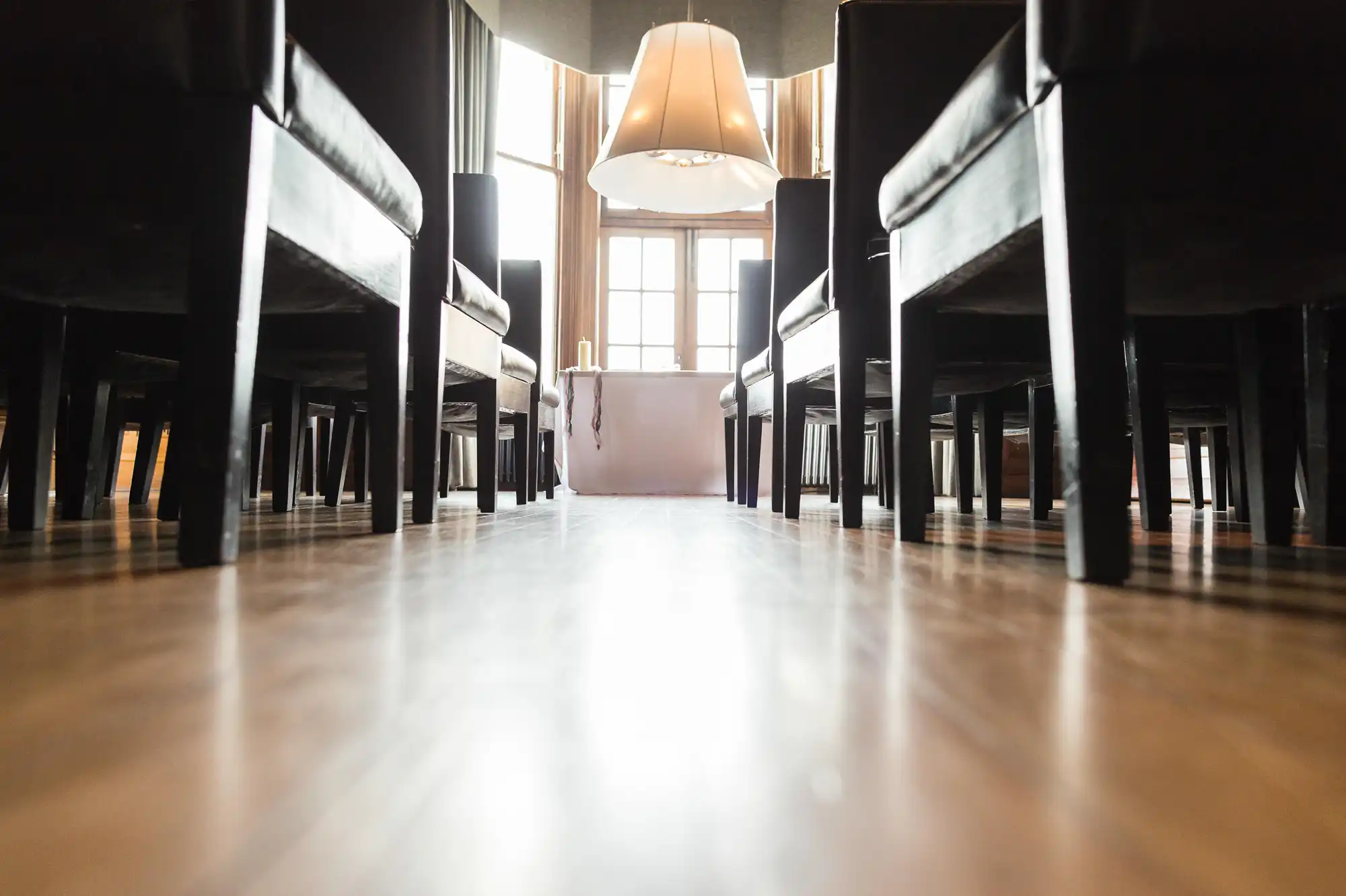 Low angle view of a room with a glossy floor, showing the underside of chairs and tables, and a pendant light hanging above. bright natural light fills the room.