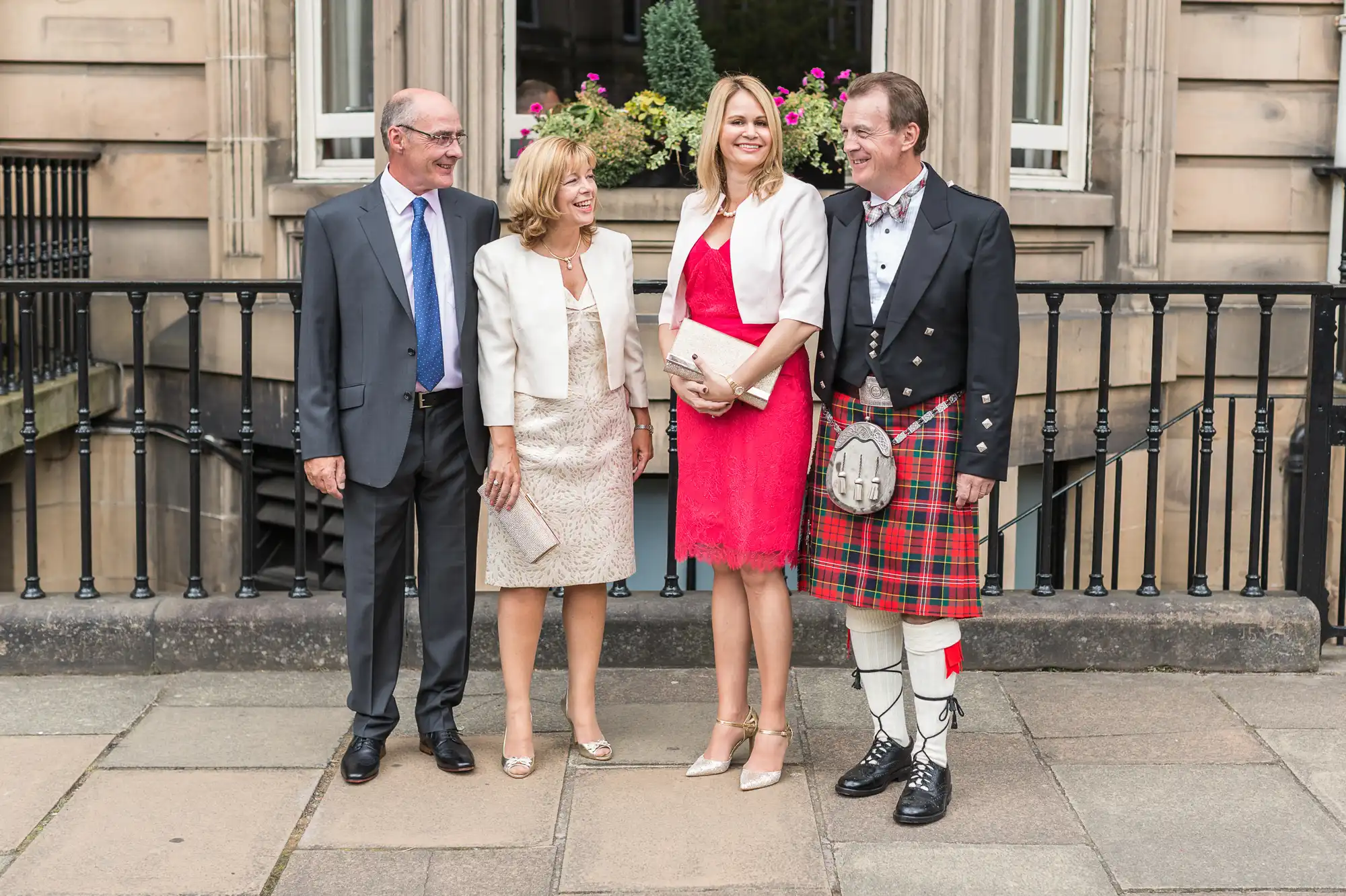 Four adults smiling at an outdoor event, two men and two women, one man wearing traditional scottish attire with a kilt.
