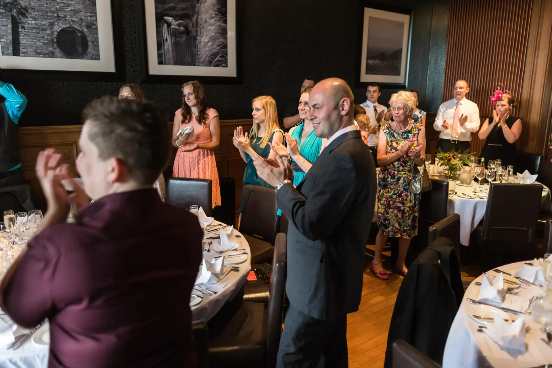 Guests standing and applauding at a festively decorated dining hall during a formal event.