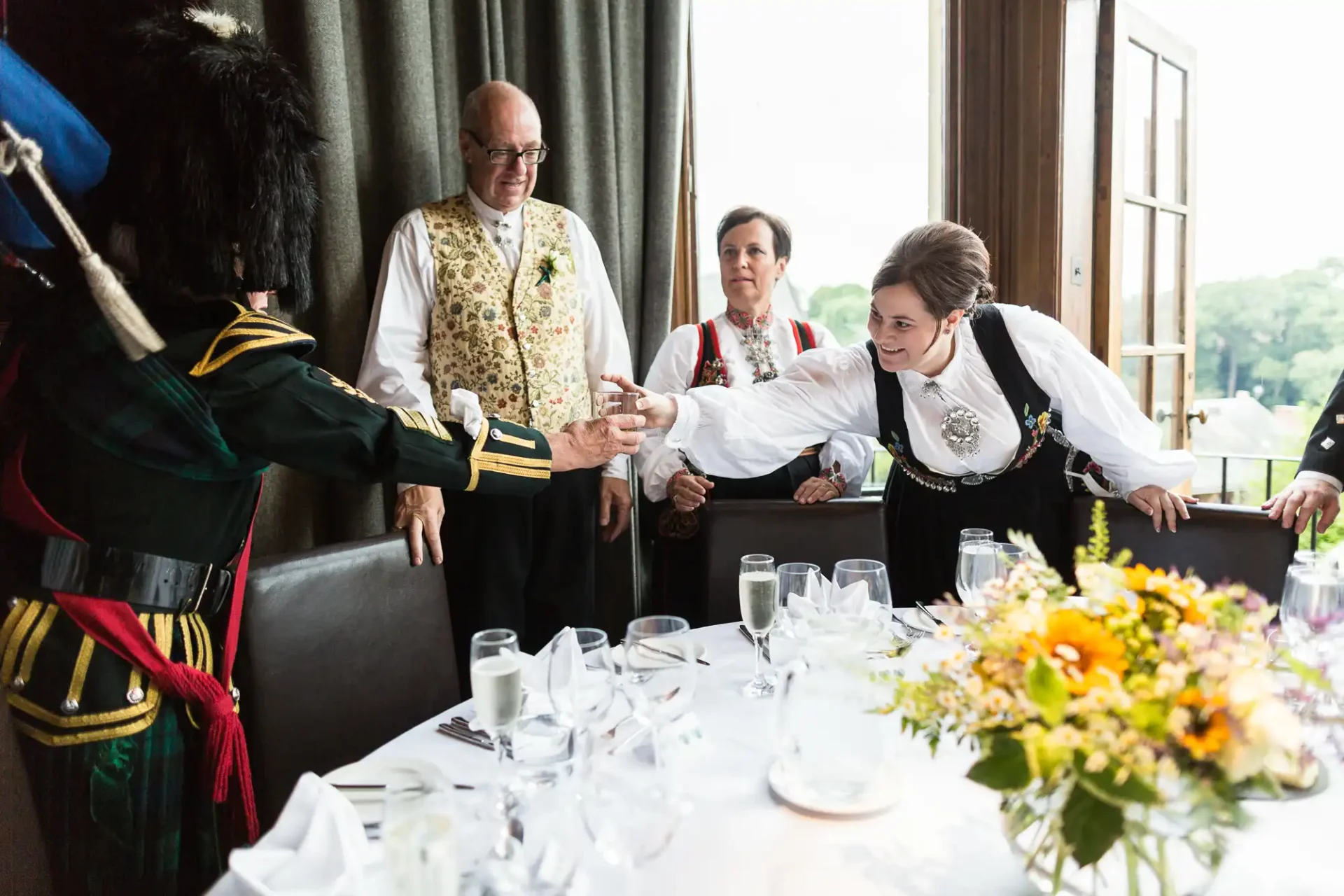 A woman in traditional dress energetically greeting a man in a historical uniform at a formal event, with two onlookers.
