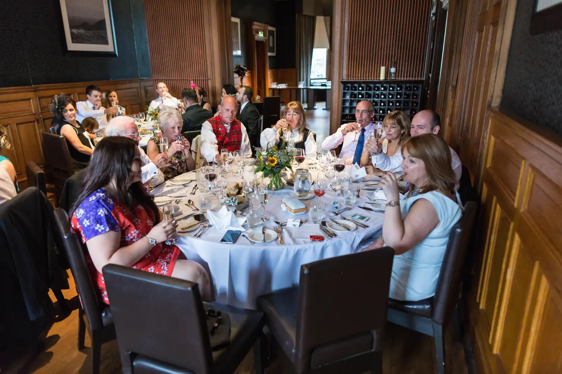 Guests seated around a dining table adorned with floral centerpieces at a formal event, engaging in conversation.