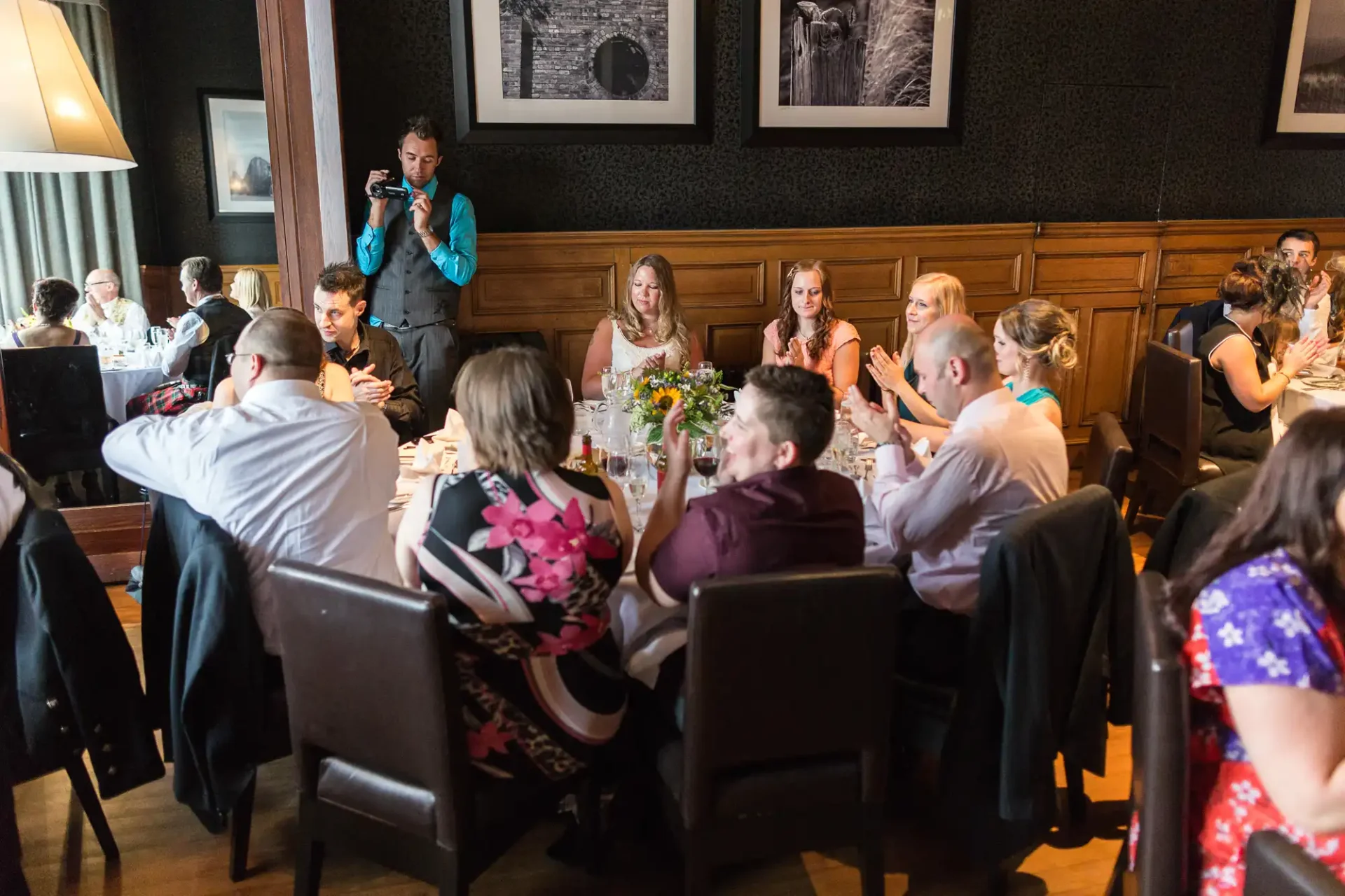 A group of people seated at a long dining table in a restaurant, with a waitperson taking orders, surrounded by dark wood panels and ambient lighting.