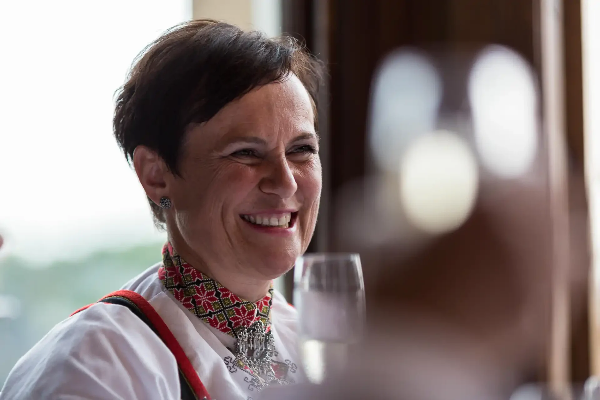 Woman in traditional embroidered blouse smiling during a conversation at a bright, indoor setting.