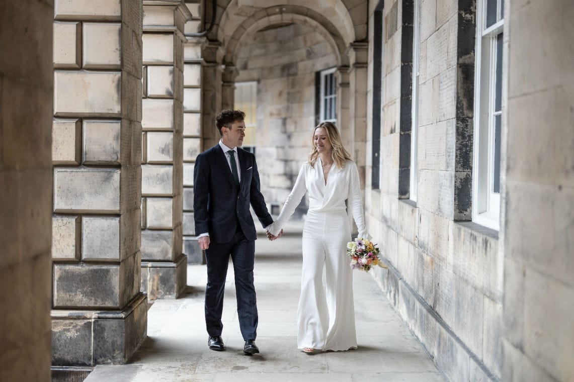bride and groom holding hands under the arches at the Signet Library