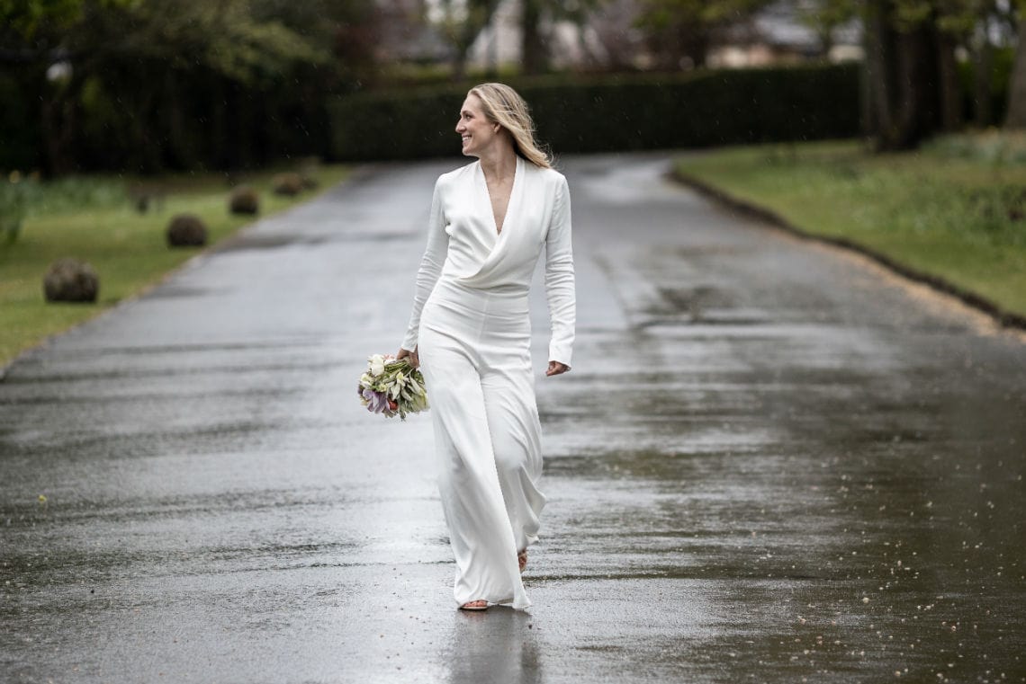 bride in a white jumpsuit walking along the avenue