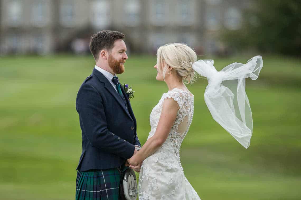 Newlyweds looking at each other in front of Dalmahoy Hotel
