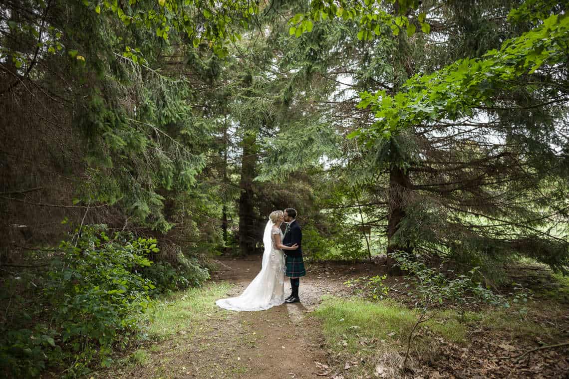 Newlyweds kissing under the trees at Dalmahoy Hotel