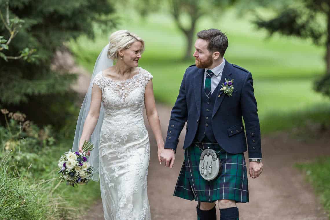 Newlyweds walking hand in hand through the grounds at Dalmahoy Hotel