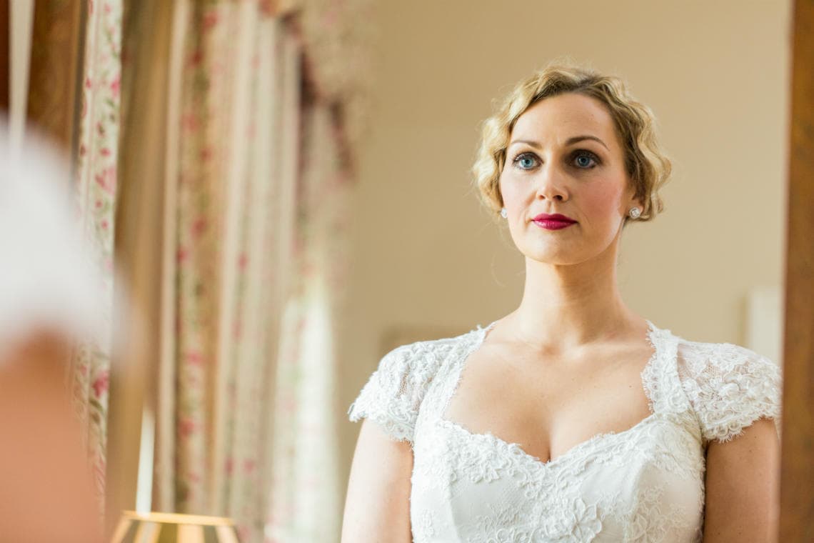 portrait of a bride in a white dress with red lipstick in front of a mirror in the Winter bedroom