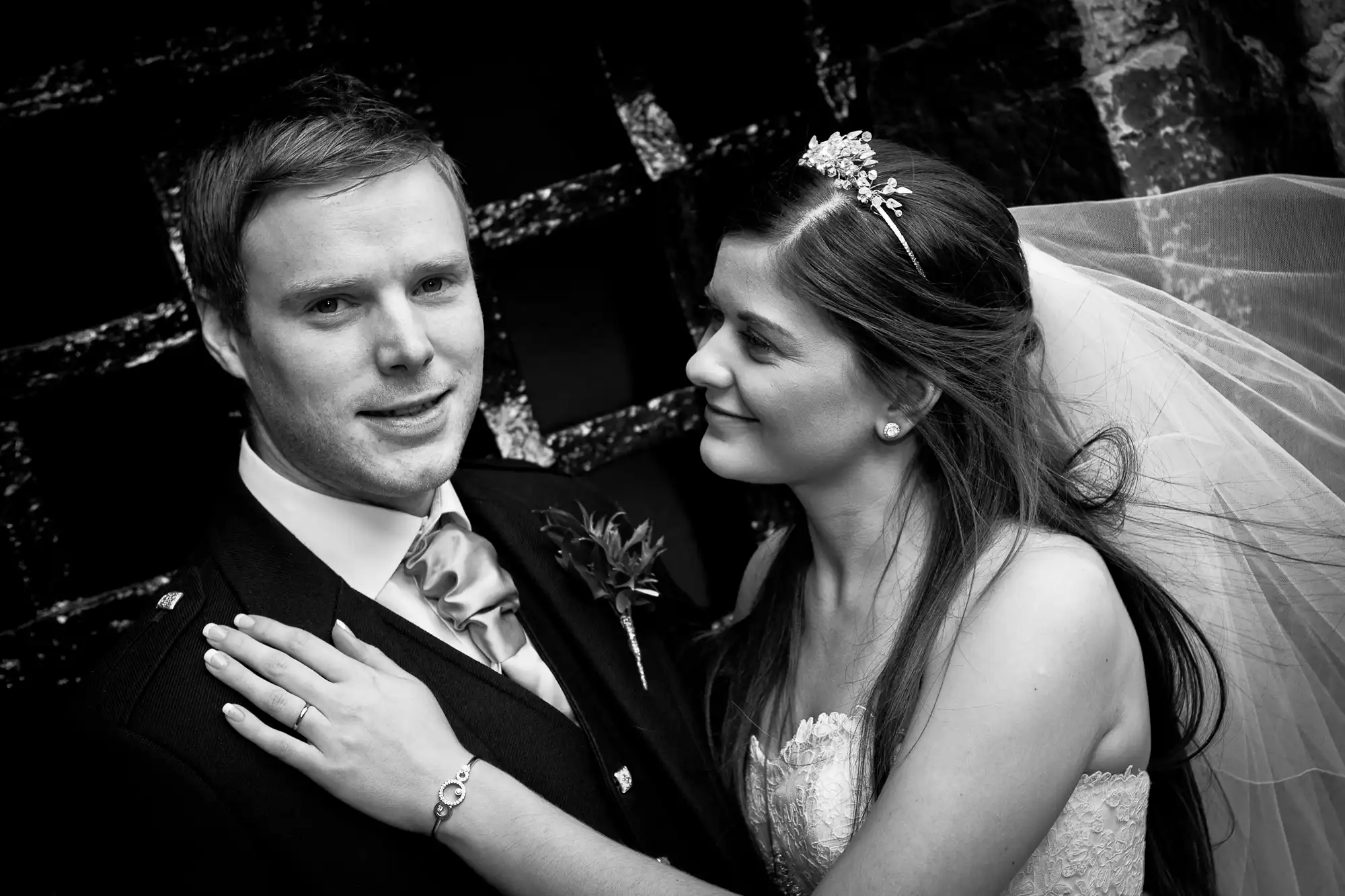 A bride and groom sharing a tender moment, the bride resting her hand on the groom's chest. both are dressed in traditional wedding attire. black and white photo.