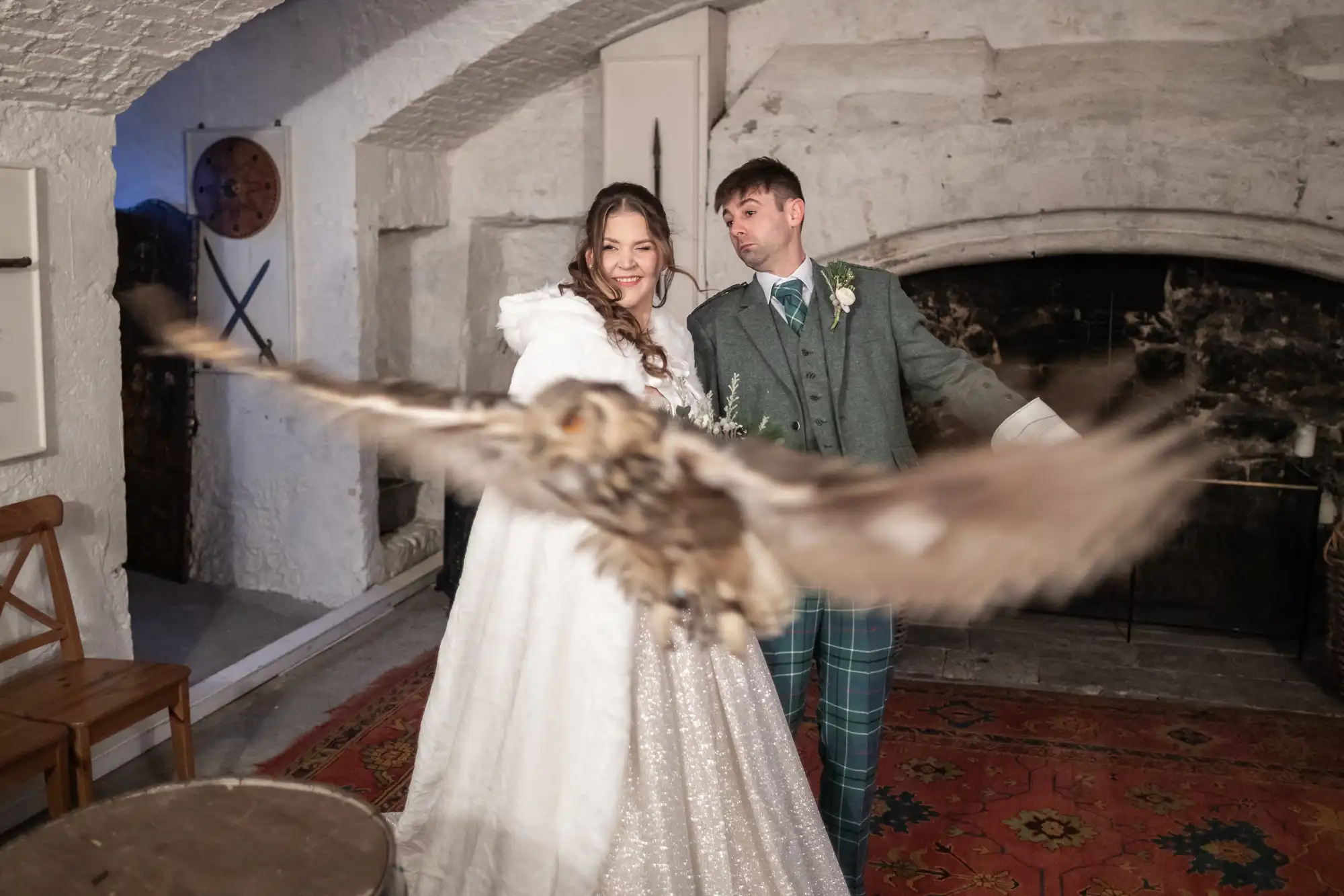 A bride and groom pose indoors while an owl flies close to the camera in front of them, captured in mid-flight by their wedding photographer at Dundas Castle.
