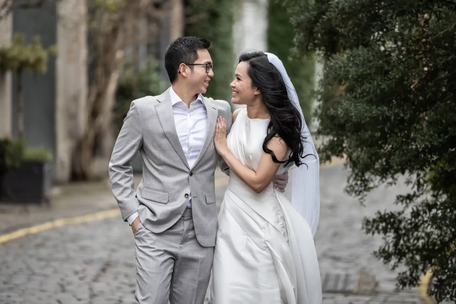 Best photo locations in Edinburgh for couples - photography tips by Jonathon Fowler Photography. Edinburgh's most Instagrammable locations featuring a couple, dressed in smart attire, smile and walk arm-in-arm on a cobblestone path lined with trees.