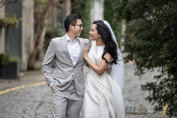 Best photo locations in Edinburgh for couples - photography tips by Jonathon Fowler Photography. Edinburgh's most Instagrammable locations featuring a couple, dressed in smart attire, smile and walk arm-in-arm on a cobblestone path lined with trees.