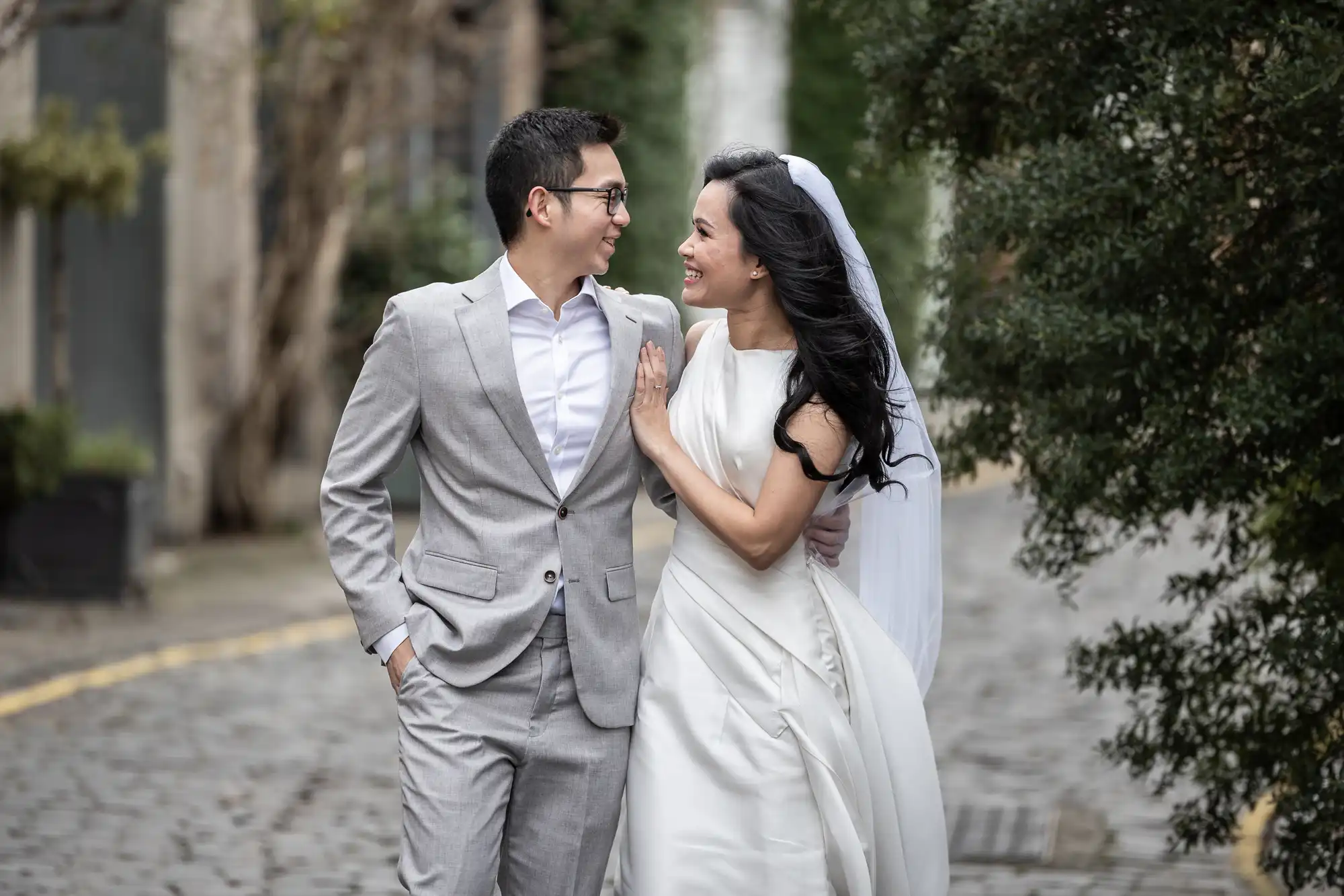 Best photo locations in Edinburgh for couples - photography tips by Jonathon Fowler Photography. Edinburgh's most Instagrammable locations featuring a couple, dressed in smart attire, smile and walk arm-in-arm on a cobblestone path lined with trees.