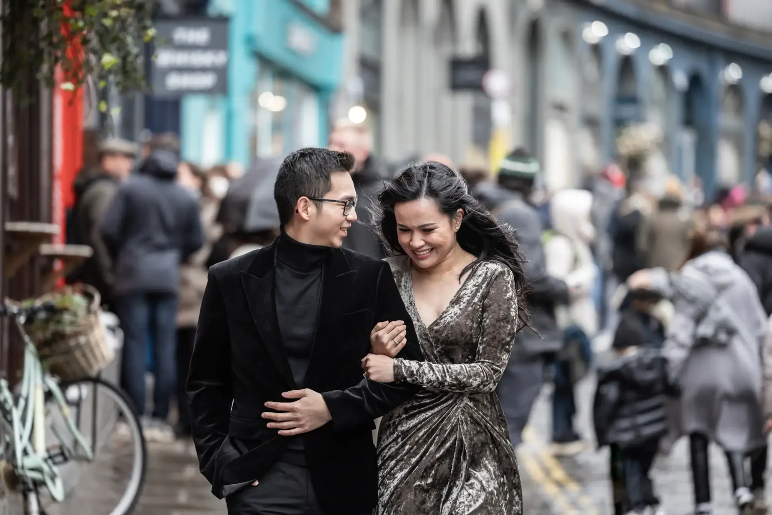 Colourful Victoria Street, one of the most Instagrammable places in Edinburgh, showing a couple, dressed formally, walks arm-in-arm down a crowded street with shops and people in the background.