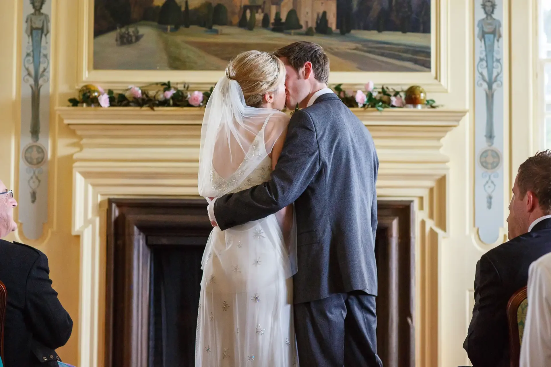 A bride and groom kissing at the altar, surrounded by elegant decor and paintings, with guests watching from the sides.