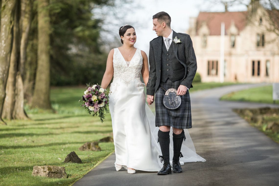 Glenbervie House wedding photographer. Newlyweds Kirsty and David walking along the driveway lined with trees.