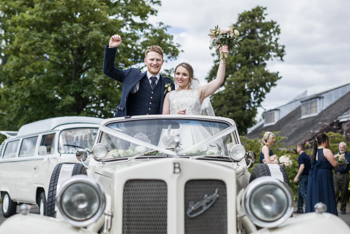 Golf course and grounds - newlyweds standing up in convertible car at the entrance