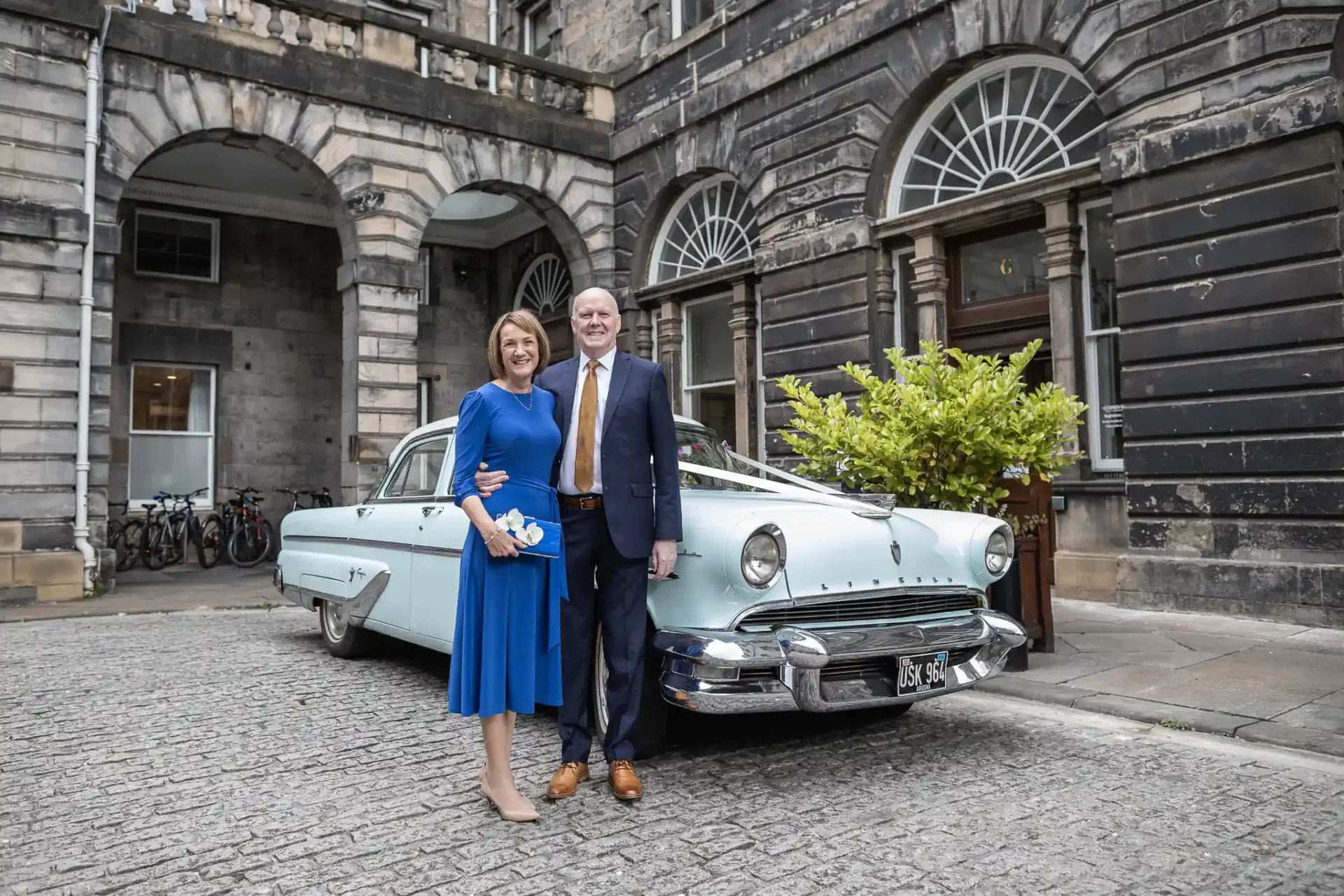 Edinburgh City Chambers weddings photo of a couple stands in front of a vintage blue car parked by a historic building.