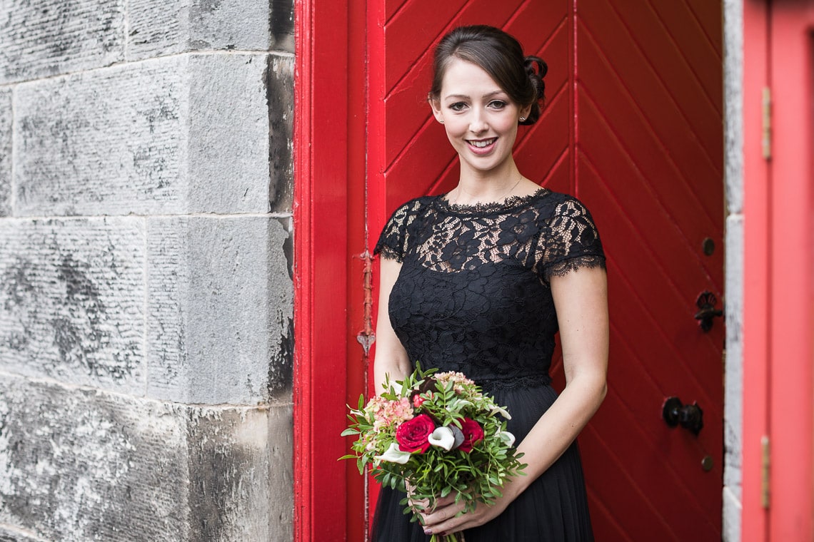 bridesmaid holding a bouquet in front of a red door at Liberton Kirk
