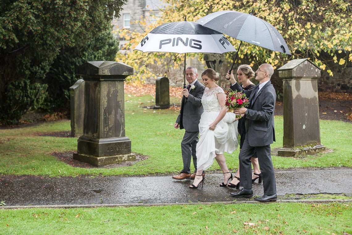 brdial party walking under umbrellas though Liberton Kirk grounds