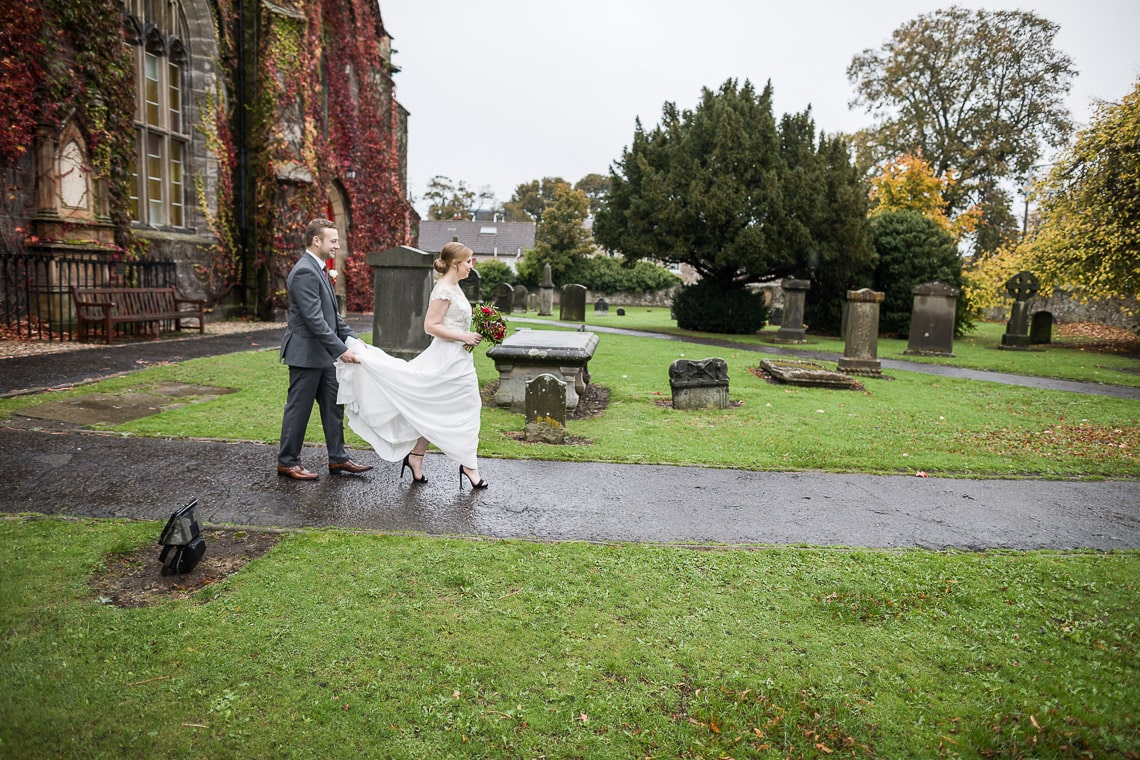 groom helps his bride walk through the grounds of Liberton Kirk
