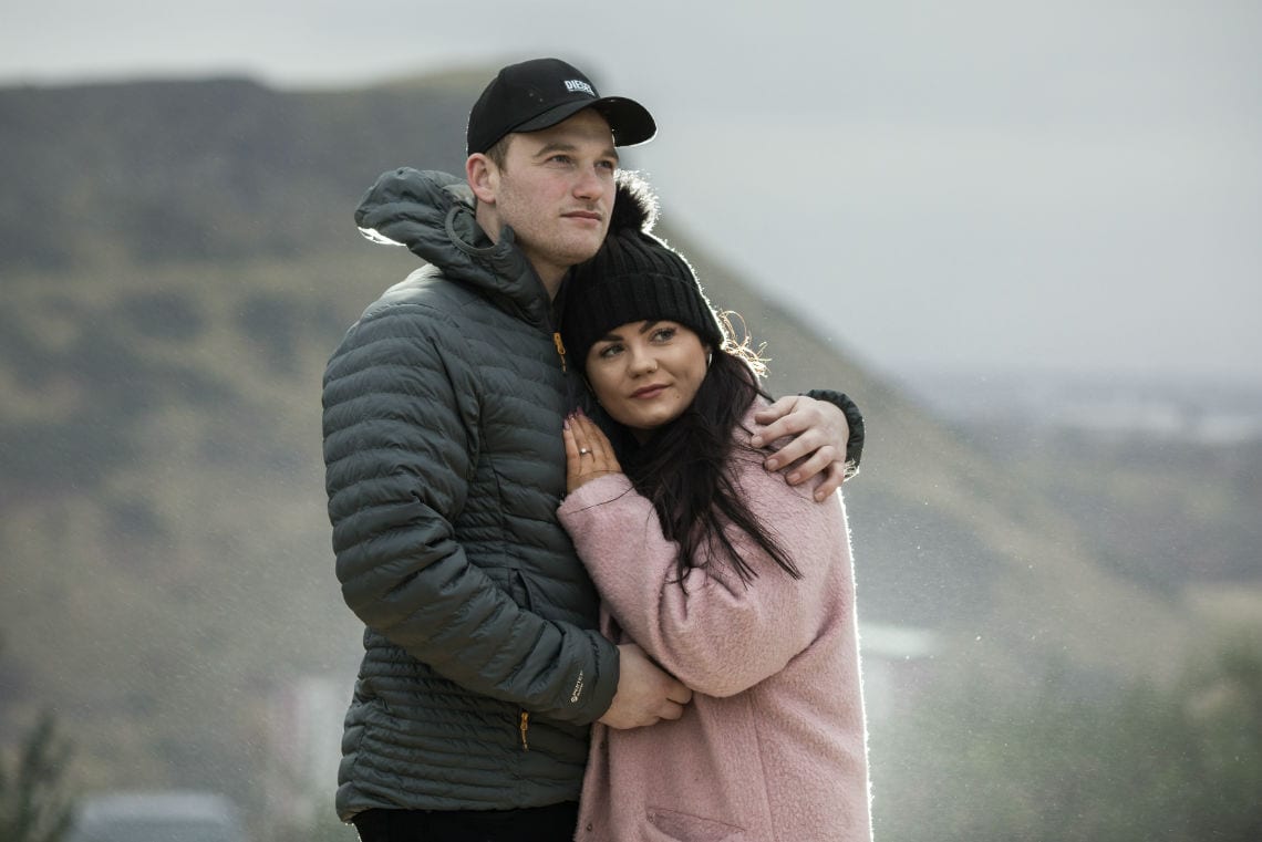 couple embrace with Salisbury Crags in the background
