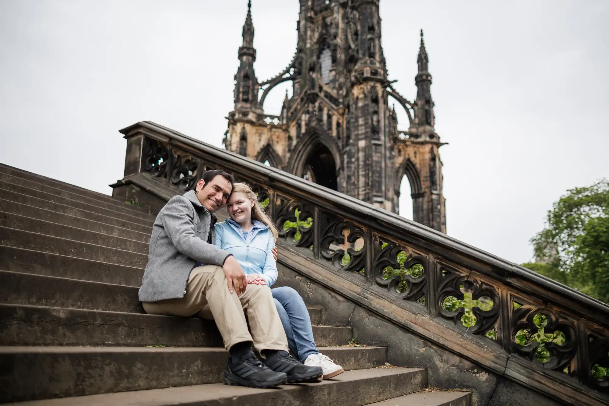 A man and woman sitting on stairs with a stone building in the background.