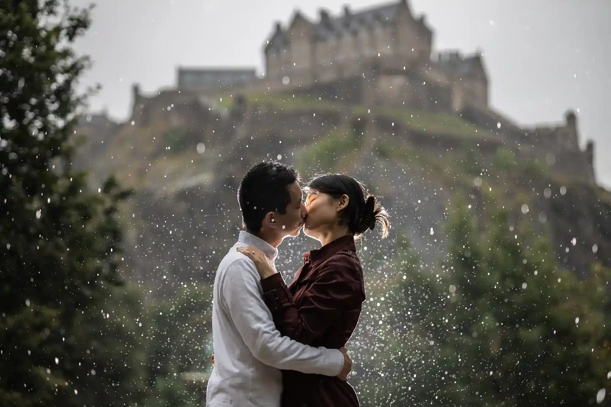A couple kisses in the rain with a blurred castle in the background.