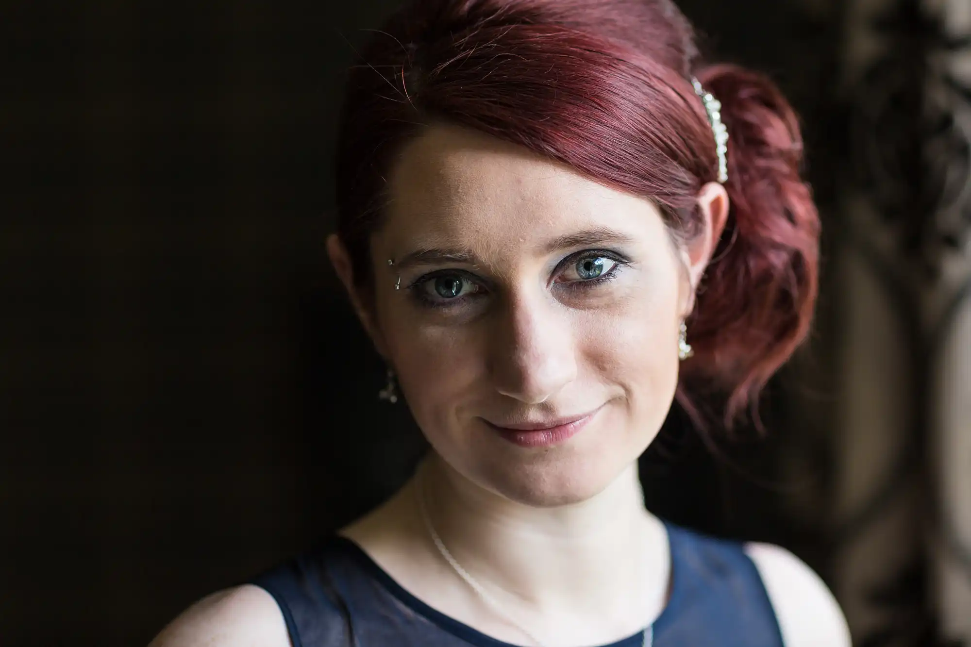 Portrait of a woman with red hair styled up, wearing a dark dress, smiling gently at the camera.