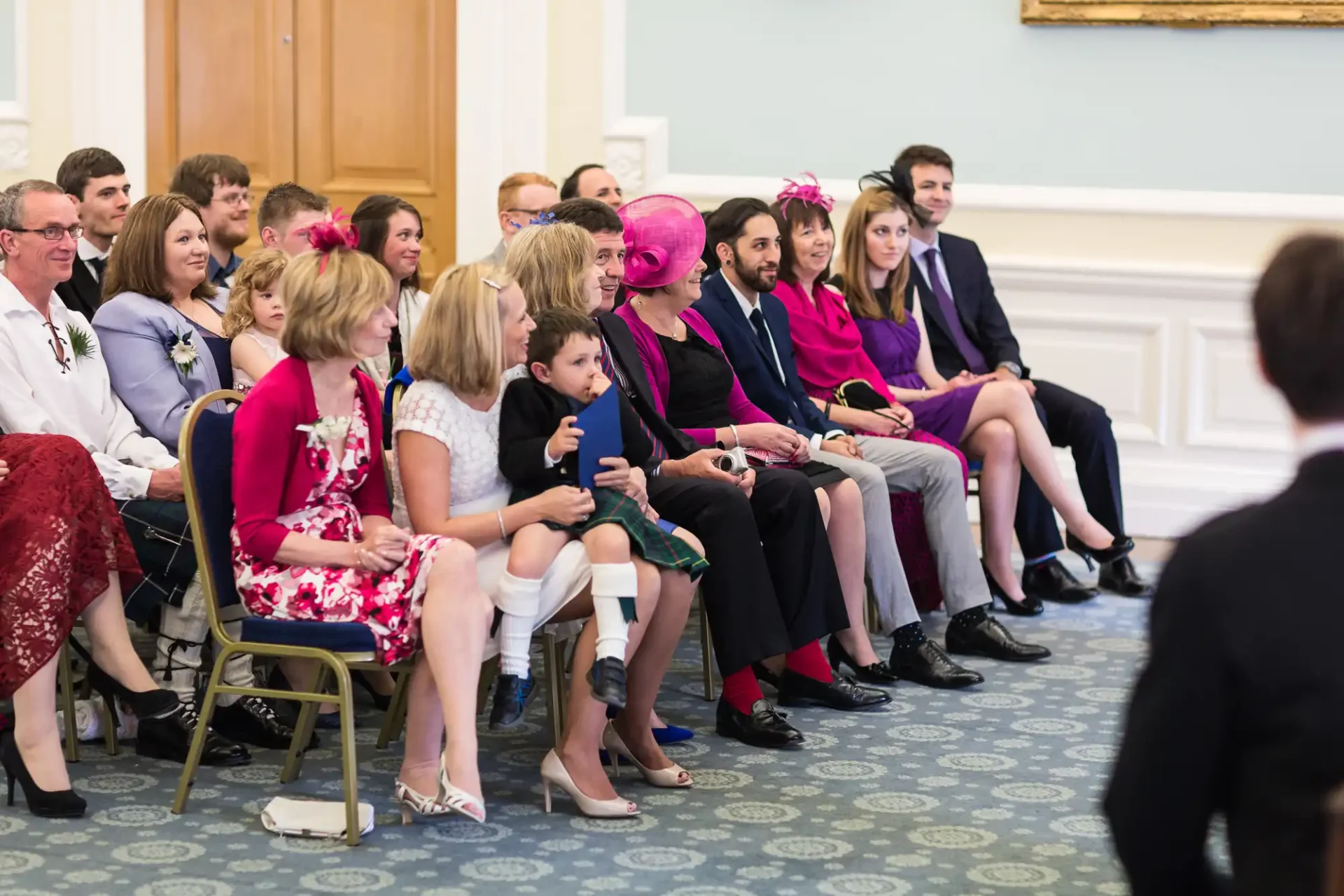 A group of people sitting in rows, attentively watching a speaker at an event, dressed in semiformal attire.