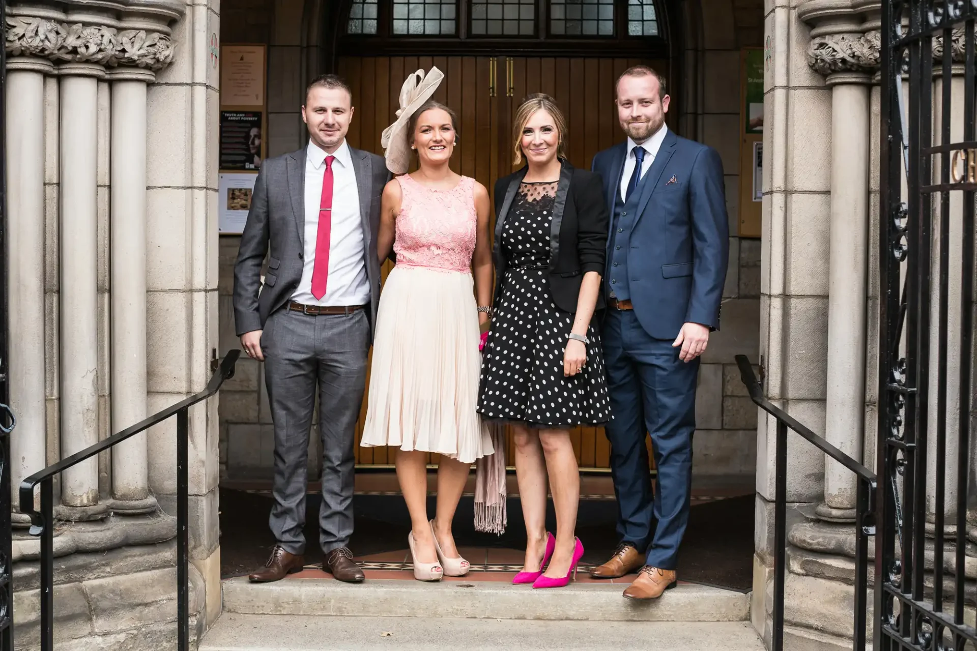 Two couples posing in formal attire on the steps of an elegant building, smiling at the camera.