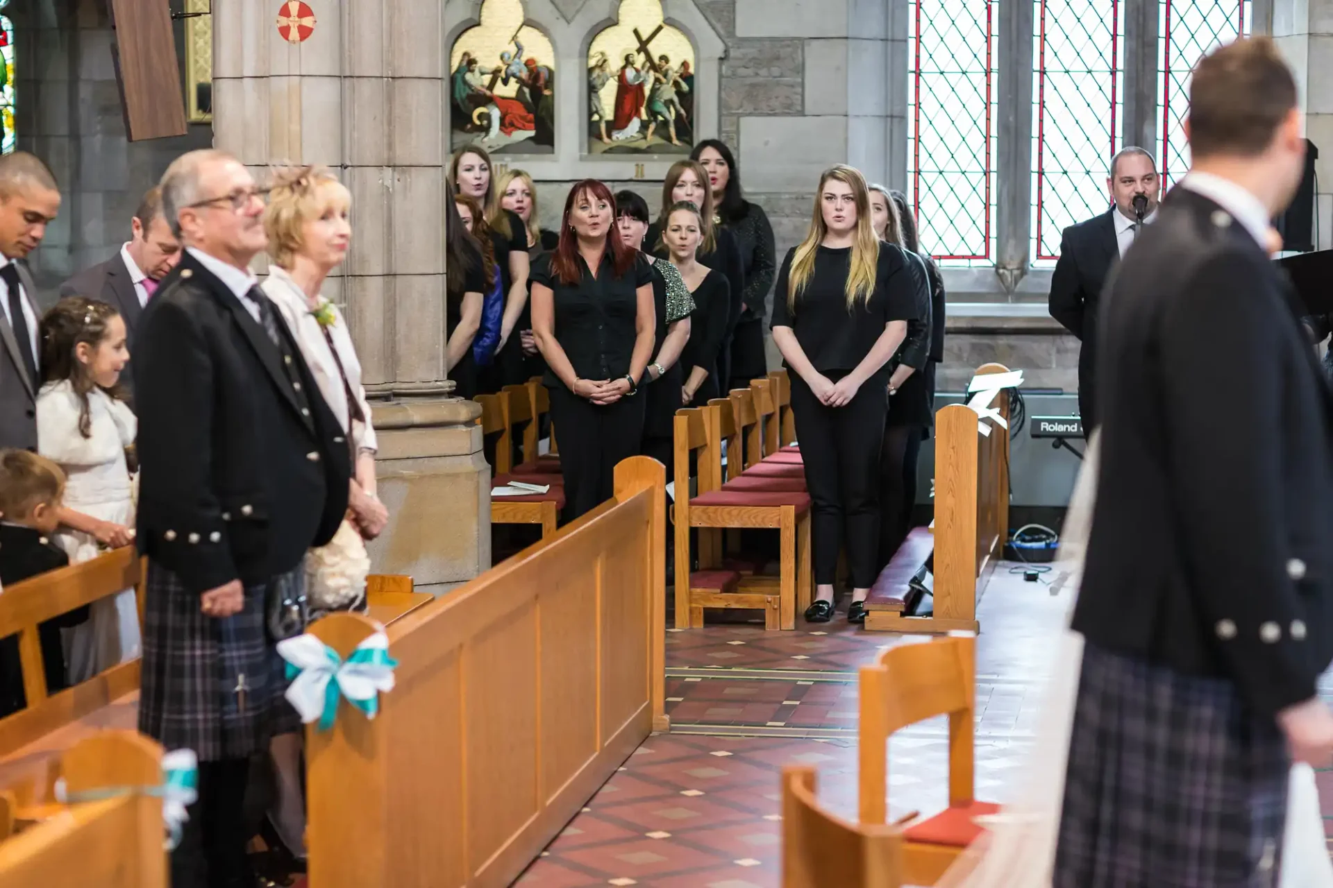 Guests standing in a church during a ceremony, some wearing formal and traditional scottish attire.