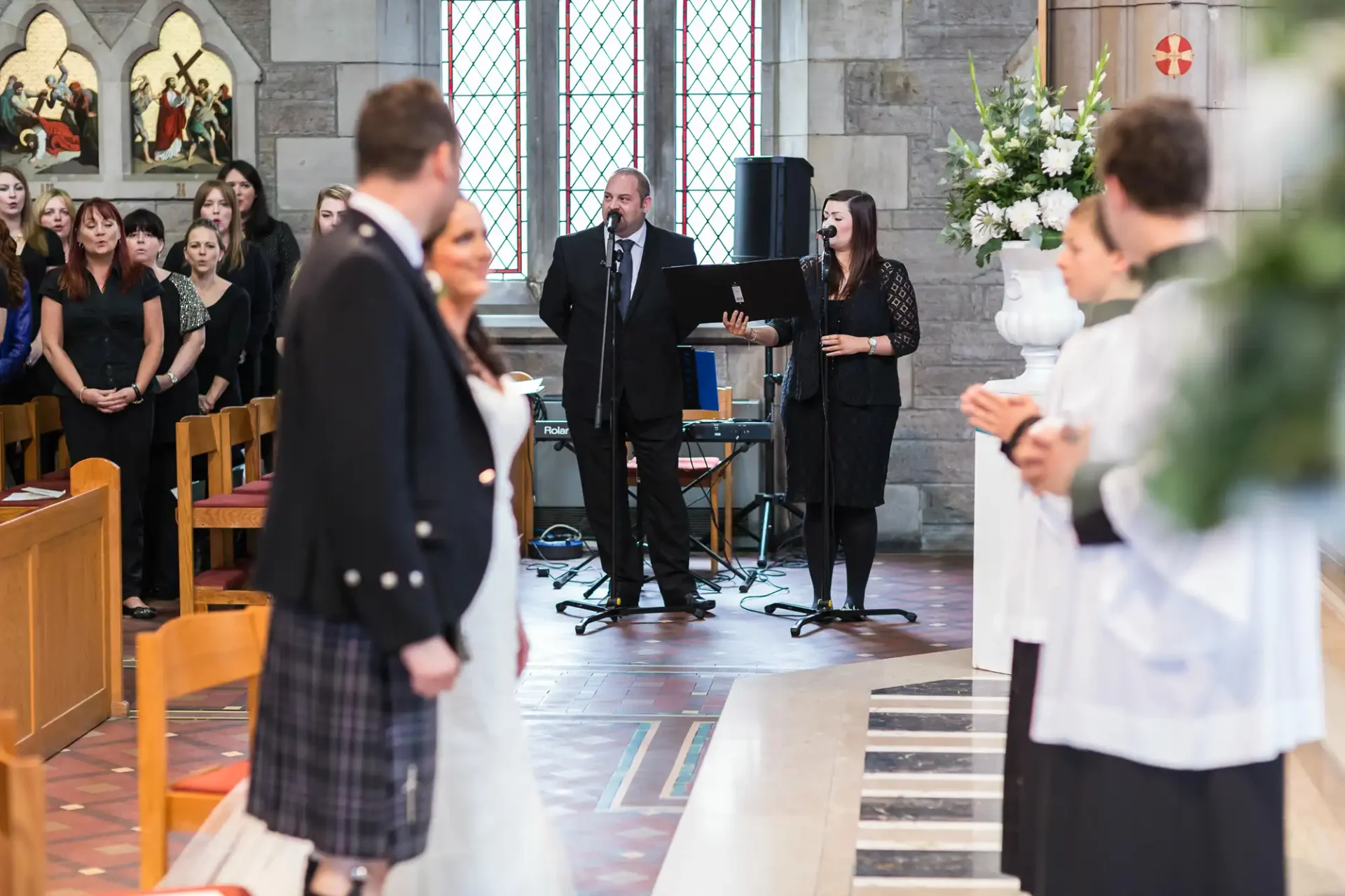 A wedding scene in a church with guests looking at a bride and groom, a band performing in the background, and colorful stained glass windows.