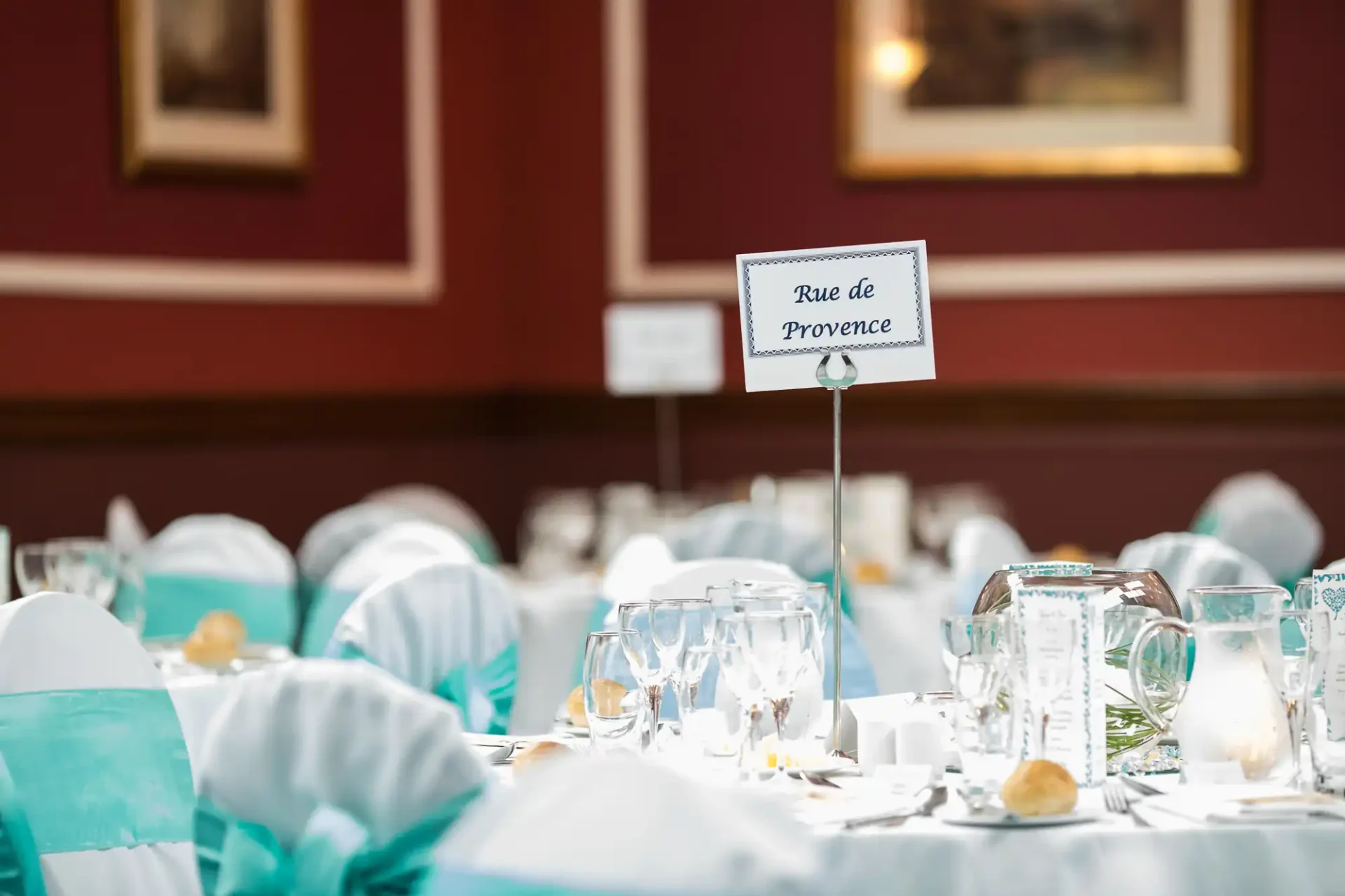 Table setting at a formal event with "rue de provence" sign, light blue chair covers, white plates, and wine glasses.