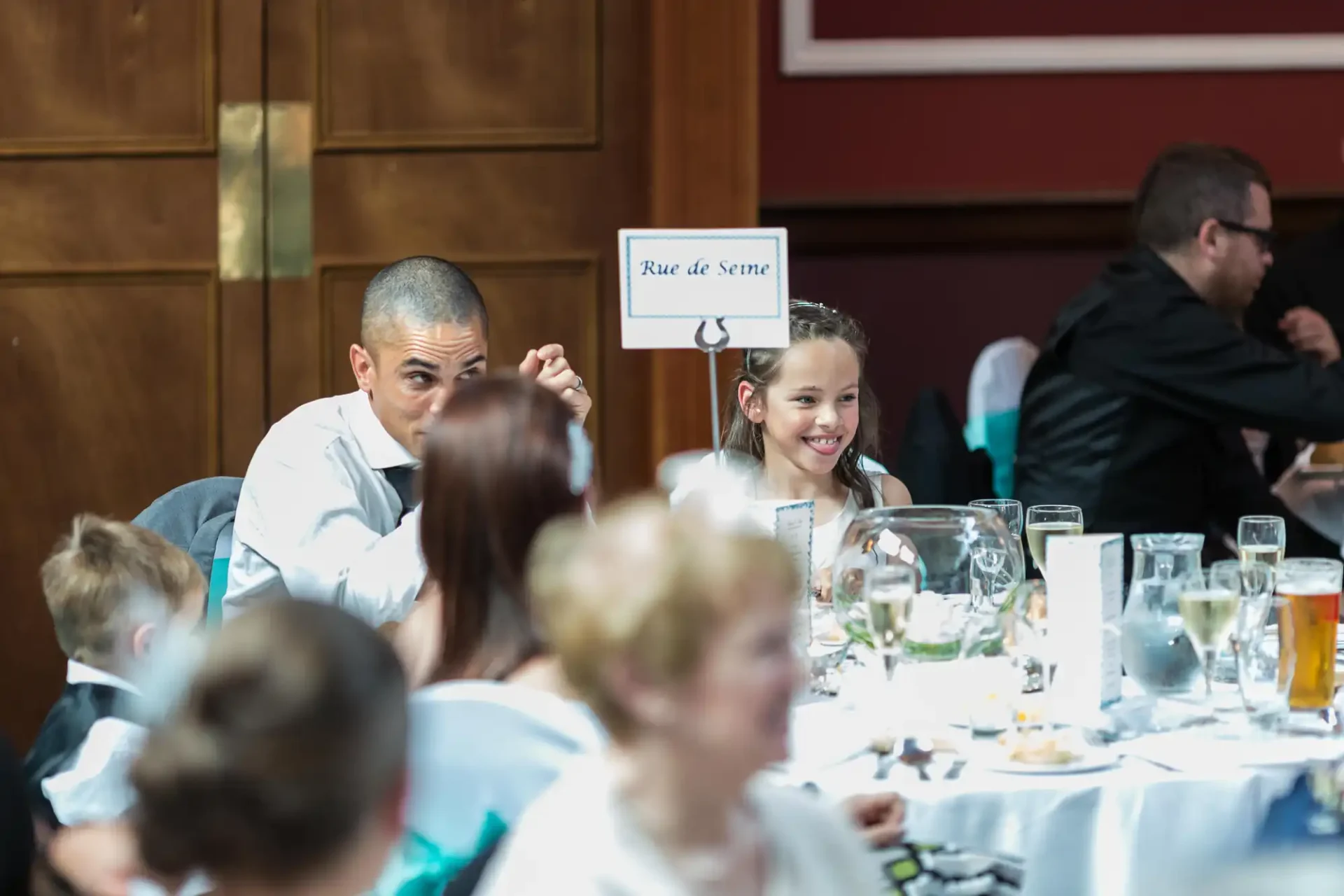 A man and a young girl smiling at each other at a banquet table, with a sign reading "rue de seine" in the background.